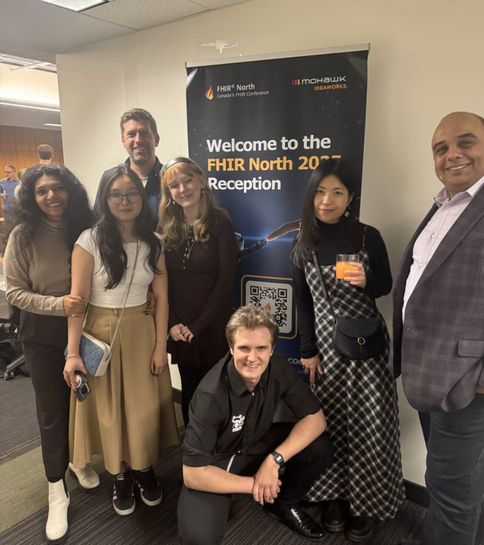 FHIR North 2025 reception — small group in front of event banner