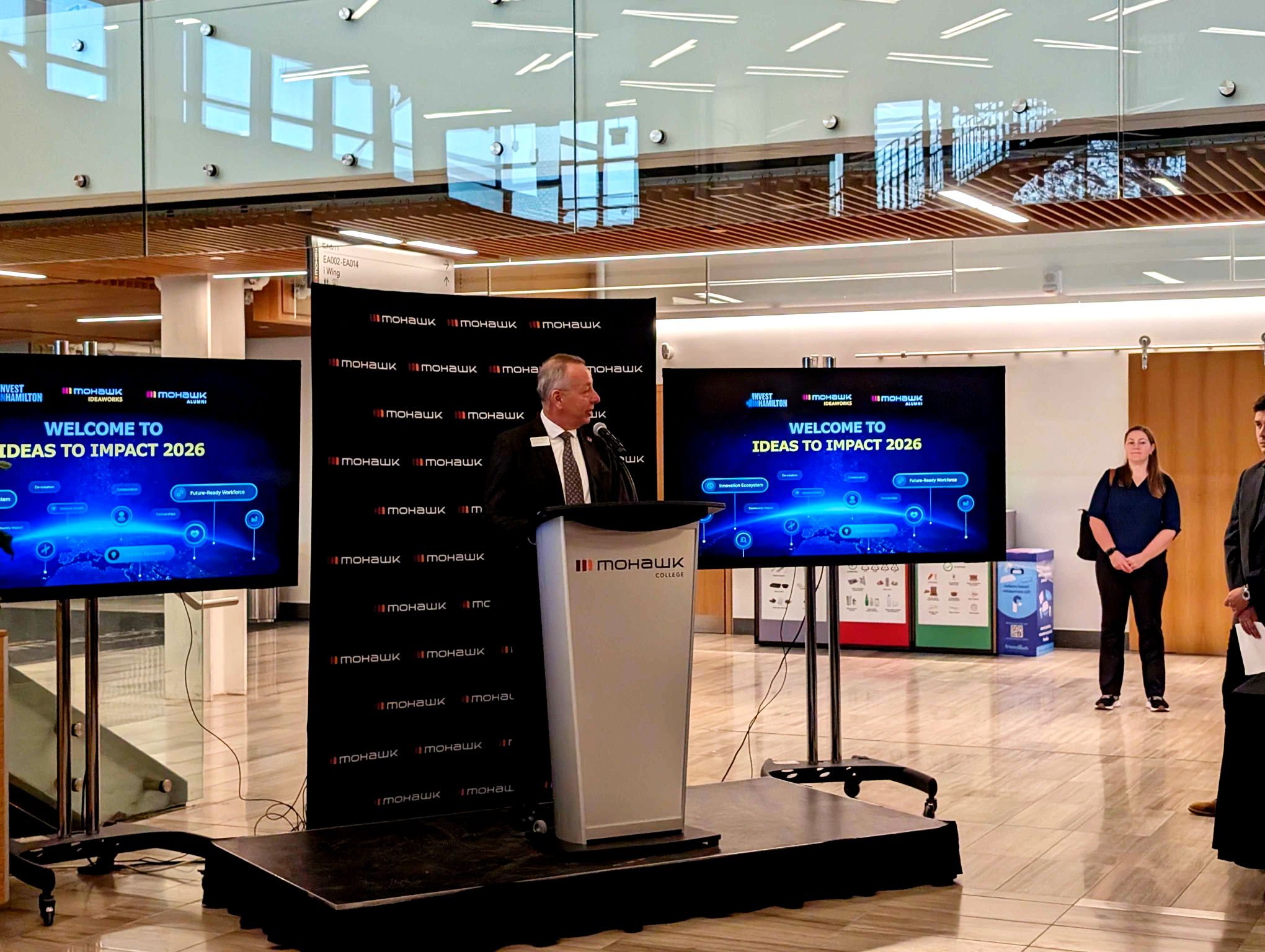 Speaker at Mohawk College Ideas to Impact 2026 welcome stage with dual screens